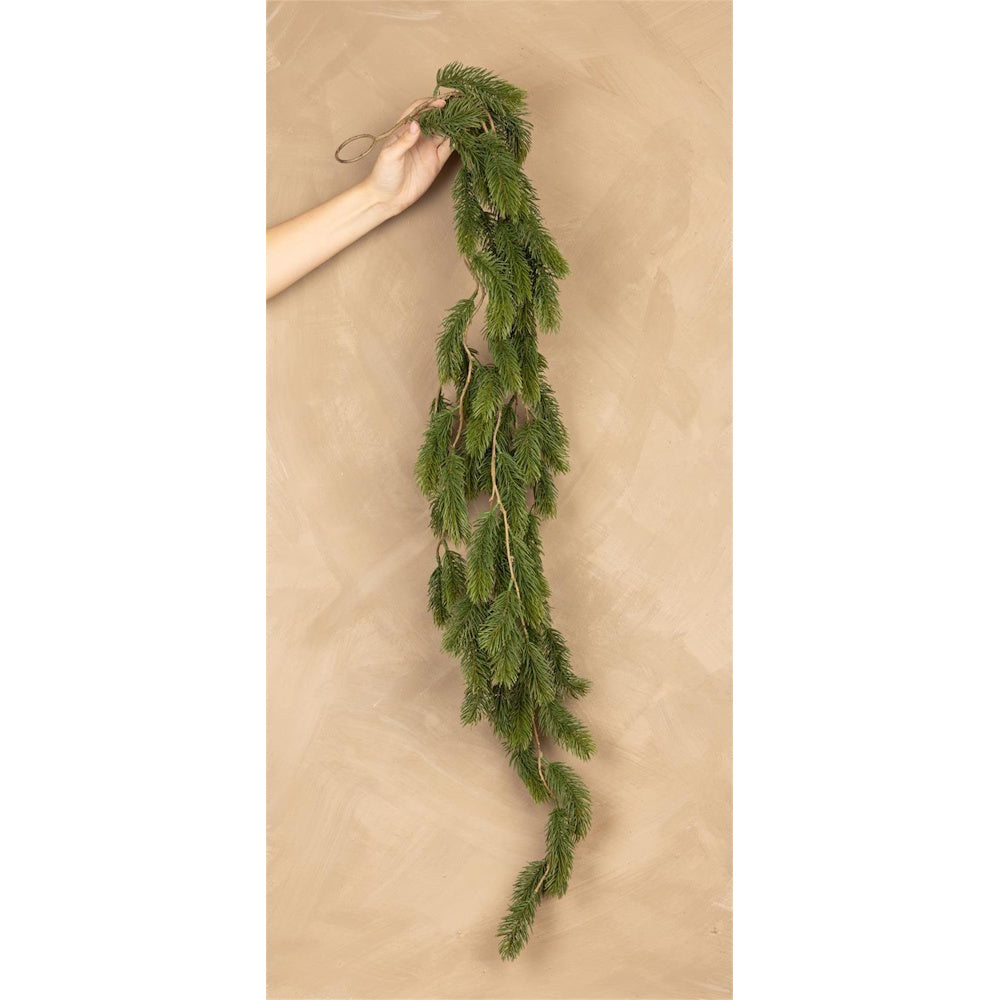 A hand holding a long, cascading artificial pine garland against a textured beige background.