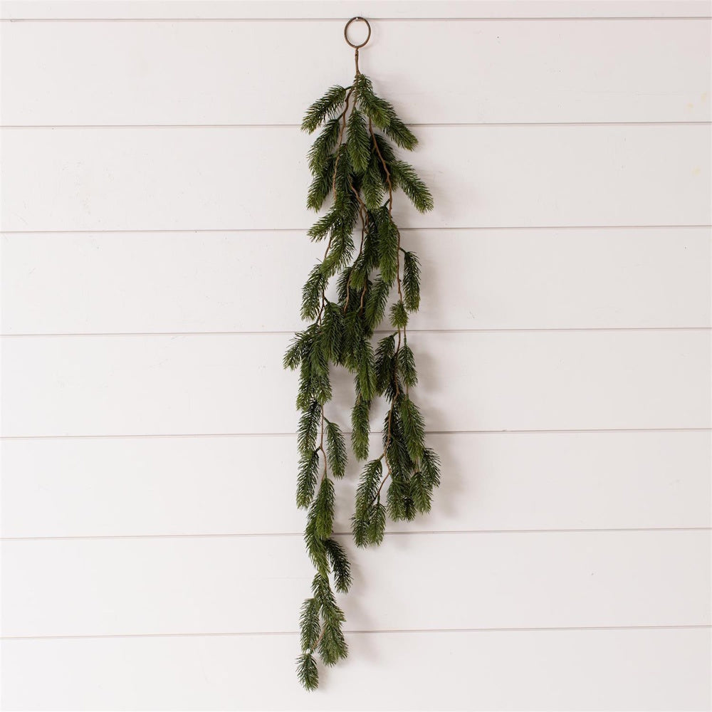 Hanging faux evergreen pine swag with a ring top on a white shiplap wall background.