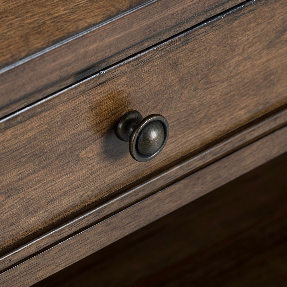 Close up of an antique bronze round knob drawer pull on a traditional brown wood coffee table drawer front.