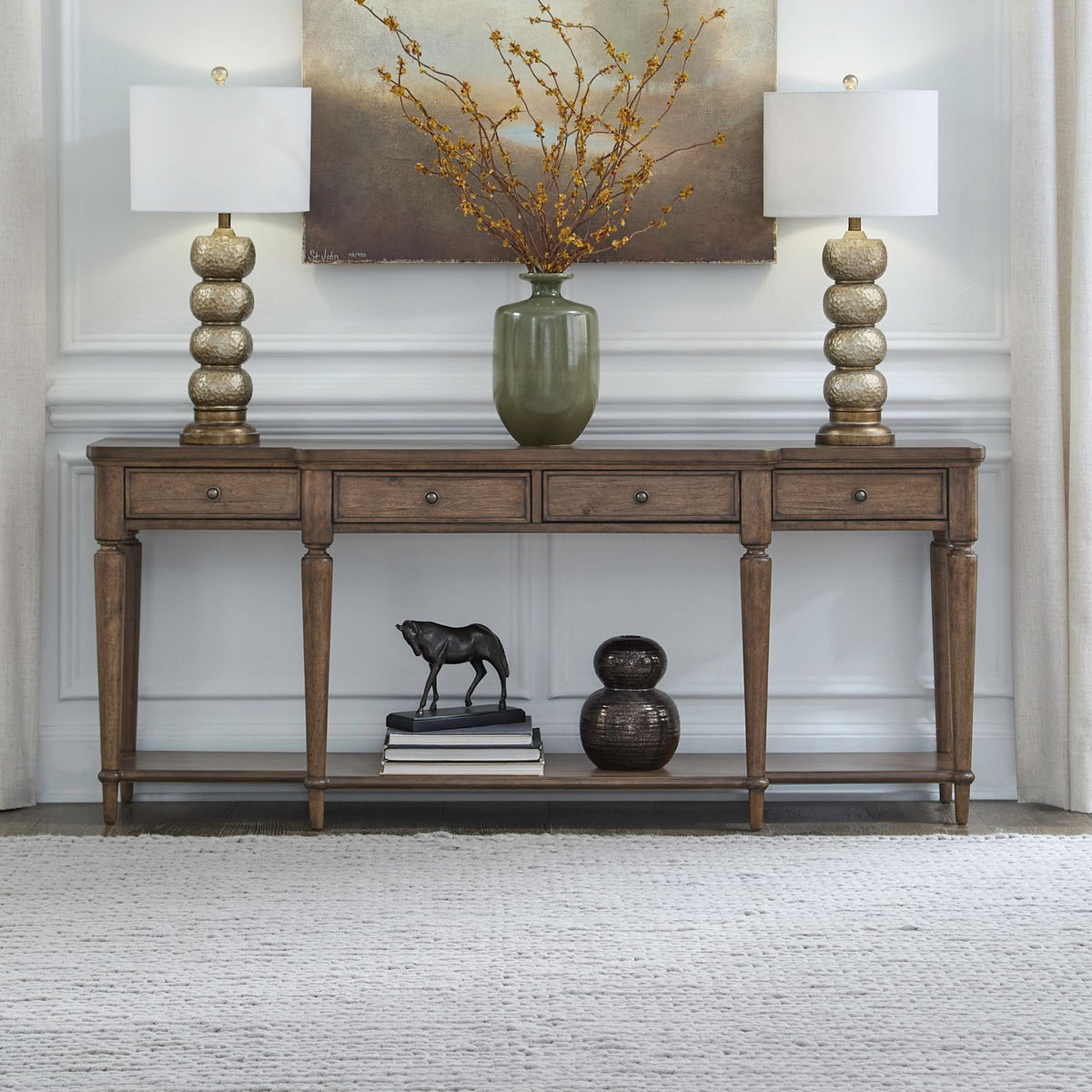 Traditional wooden long console table with drawers and bottom shelf styled with lamps and decor.