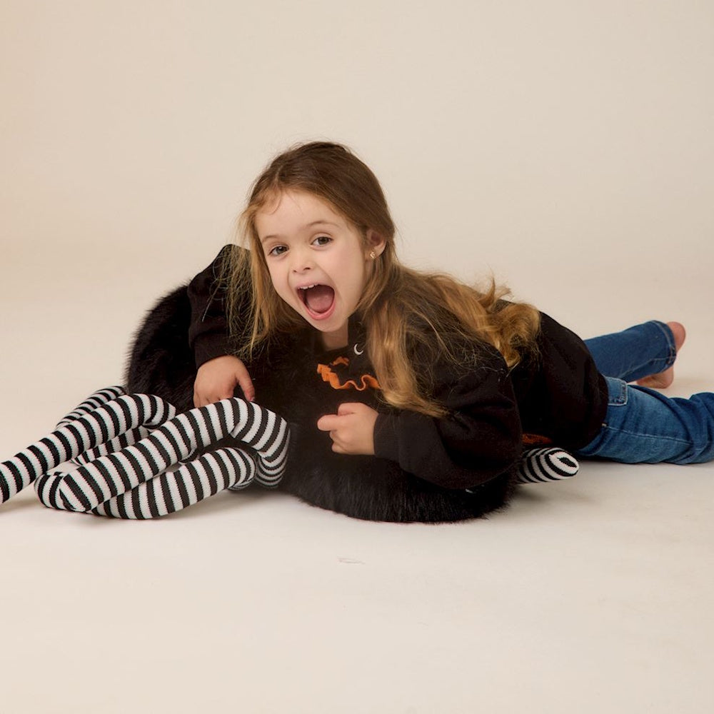 Young girl lying on floor hugging a large plush spider with black-and-white striped legs.
