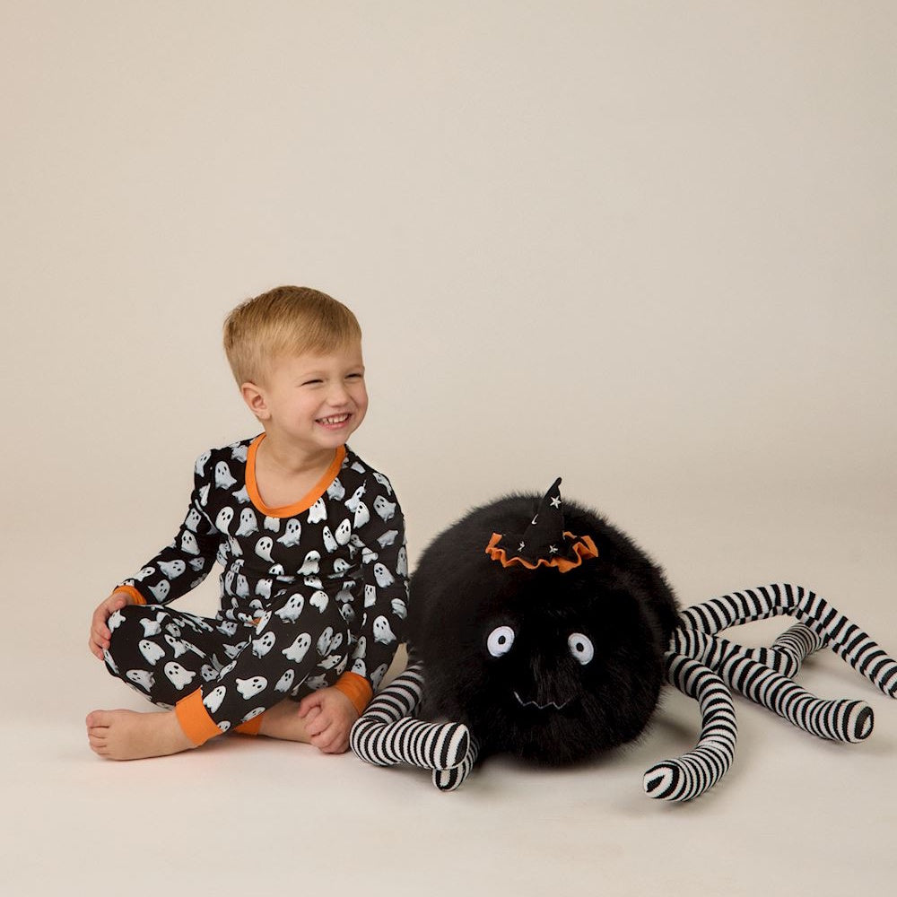 Smiling toddler in ghost pajamas sitting next to a large plush spider with striped legs.