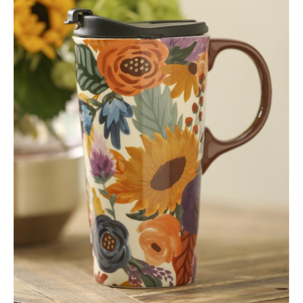 A ceramic travel mug with a vibrant autumn floral pattern, a brown handle, and a black lid on a table.
