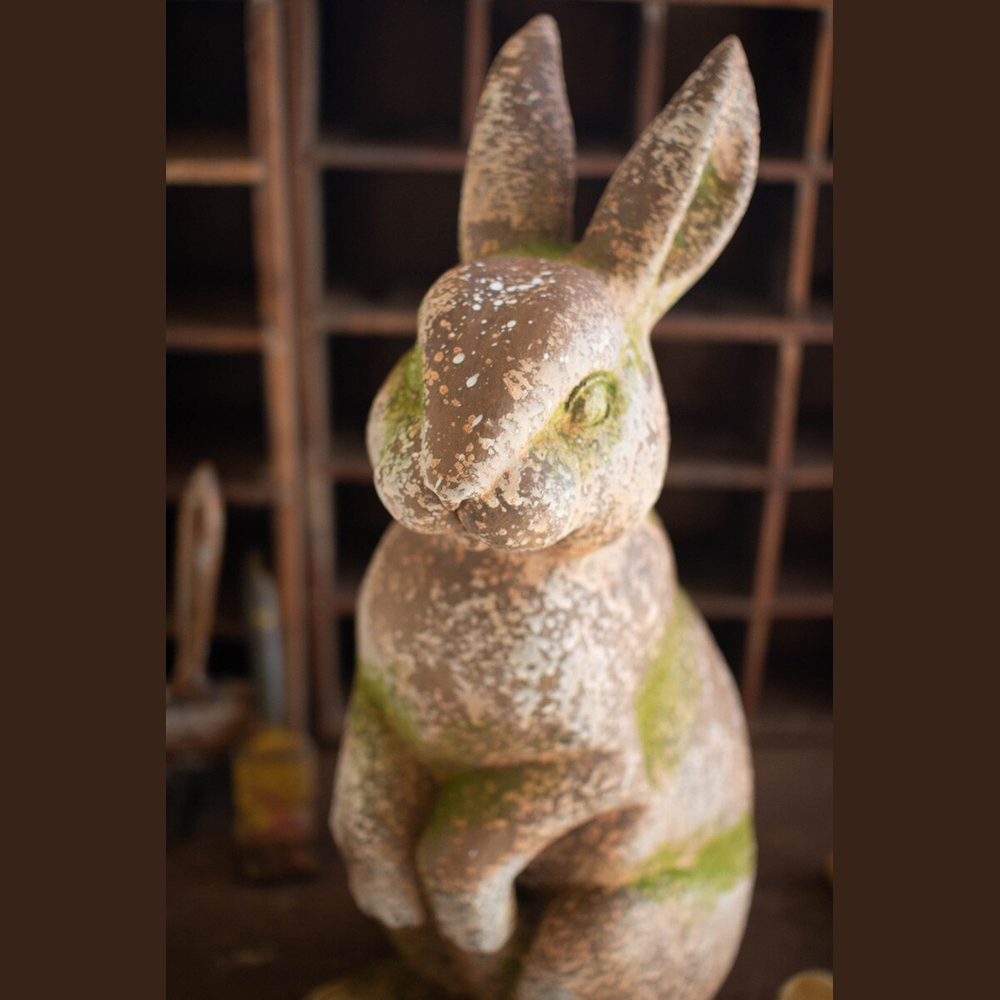 Rustic weathered rabbit garden statue with faux moss and concrete finish in a vintage wooden cubby background.