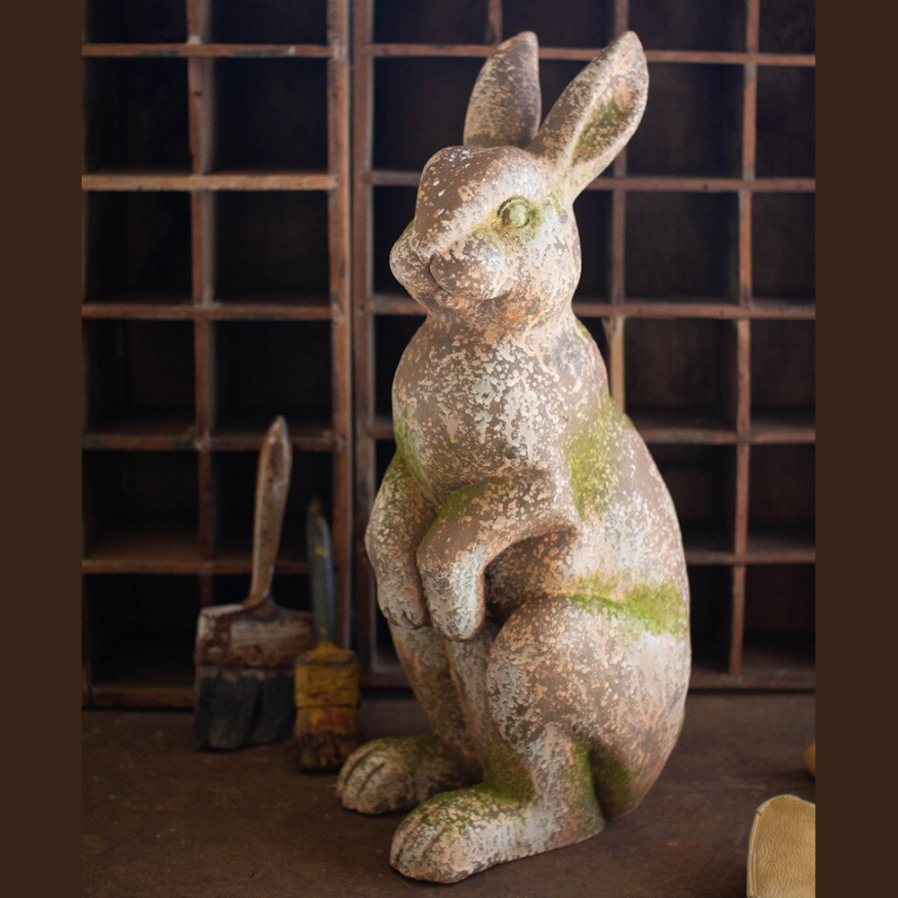 Vintage-style faux concrete rabbit statue with weathered texture and moss accents on a rustic wooden background.