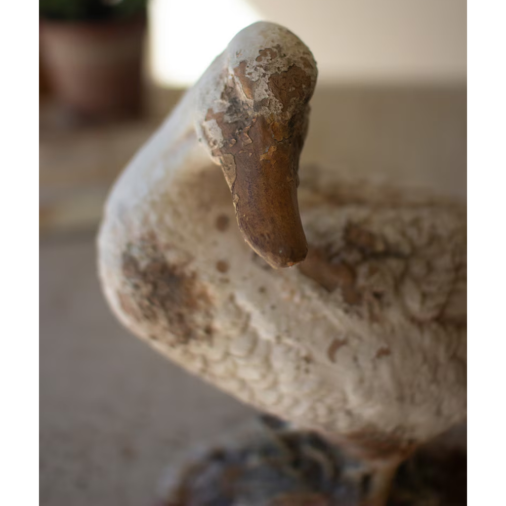 Close-up view of a rustic duck statue featuring a weathered, distressed finish on its head and bill.