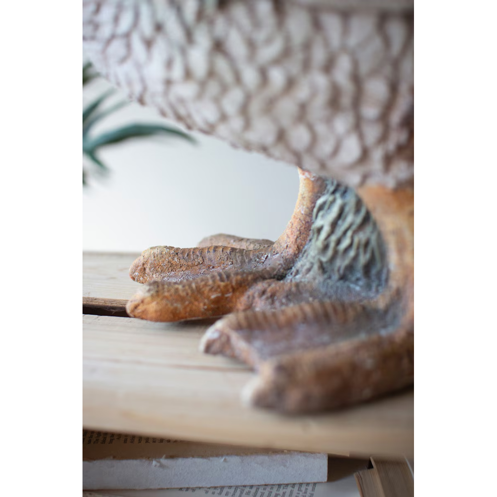 Close-up of the textured webbed feet of a faux-concrete duck statue resting on a wooden surface.