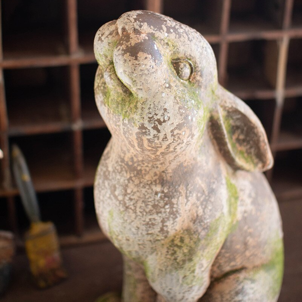 Weathered faux concrete rabbit statue with realistic moss patina and vintage distressed finish in a rustic garden setting.