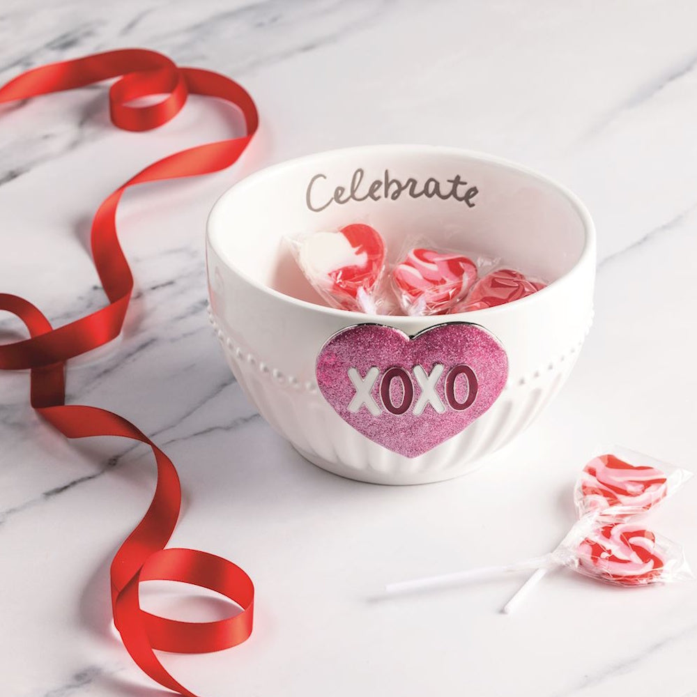White ceramic "Celebrate" bowl with pink glitter XOXO charm, red ribbon, and heart lollipops.
