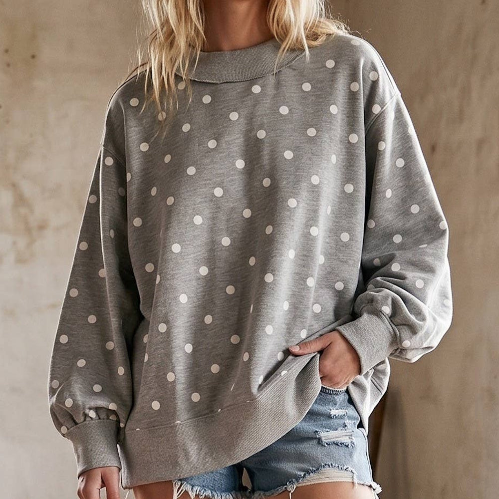Woman wearing an oversized heather grey crewneck pullover with a white polka dot pattern and distressed denim shorts.