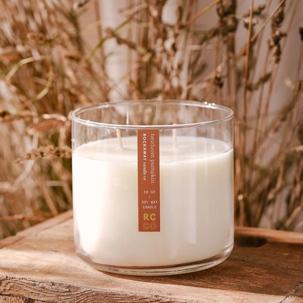 A 16 oz cream-colored soy wax candle in a clear glass jar, resting on a wooden surface with a rustic background.
