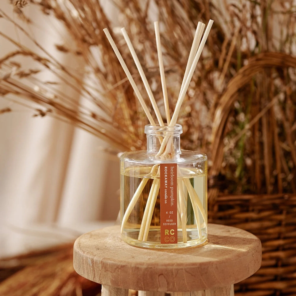 Rockaway Candle Co. Heirloom Pumpkin reed diffuser in a glass bottle on a wooden stool with fall decor.
