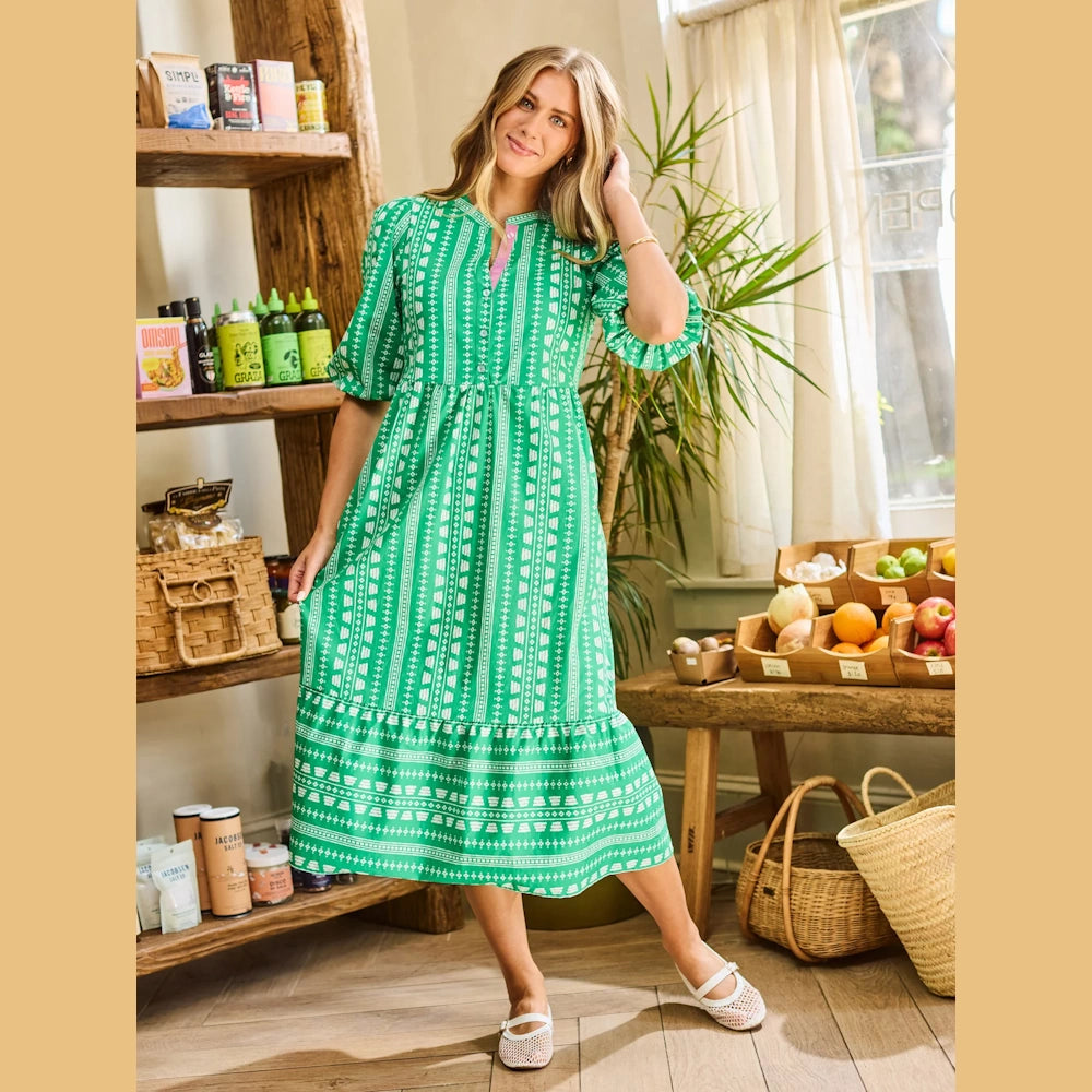 Woman in a green patterned midi dress with puff sleeves and white mesh flats in a rustic market setting.