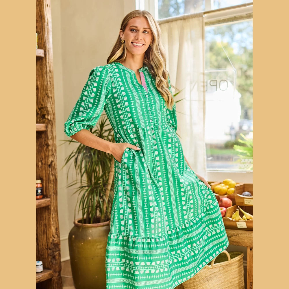 Woman in a green patterned midi dress with three-quarter sleeves, pockets, and a white geometric heritage stitch print.