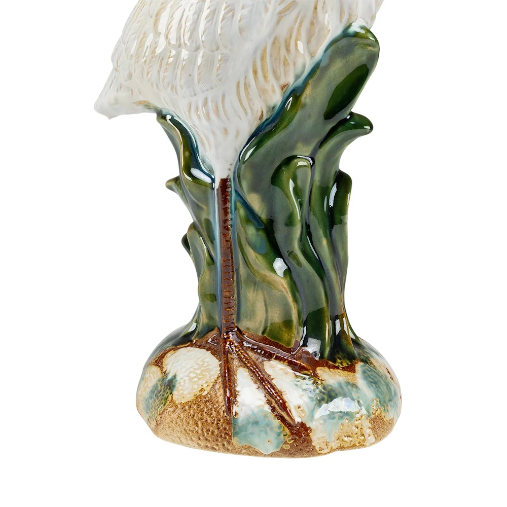 Close-up of a ceramic heron figurine base showing its brown leg and webbed foot resting on a textured mound.