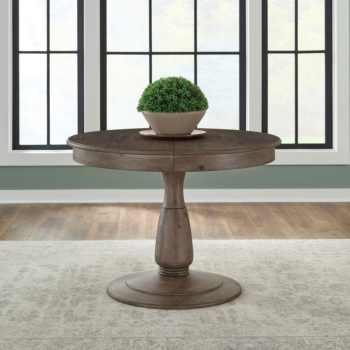 Round pedestal dining table made of dark wood with a potted plant on top, placed on a beige rug.