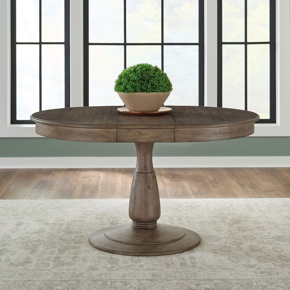 Hickory Grove round wooden pedestal dining table with a green plant centerpiece in a bright room.