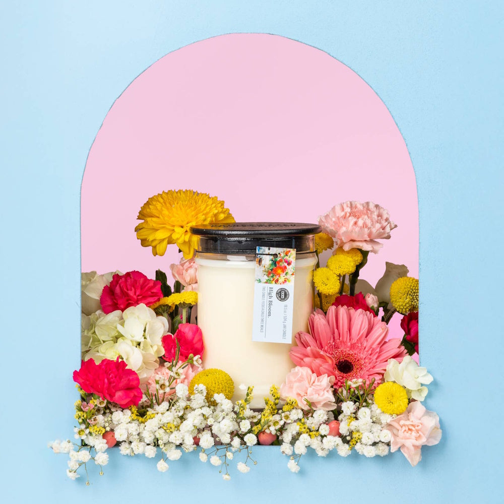 High Bloom jar candle surrounded by colorful chrysanthemums, dahlias, and carnations in a pink and blue arched frame.