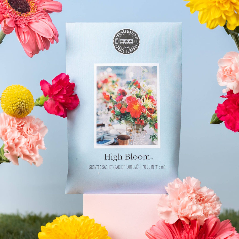 Bridgewater Candle Company High Bloom scented sachet surrounded by colorful pink and yellow spring flowers.