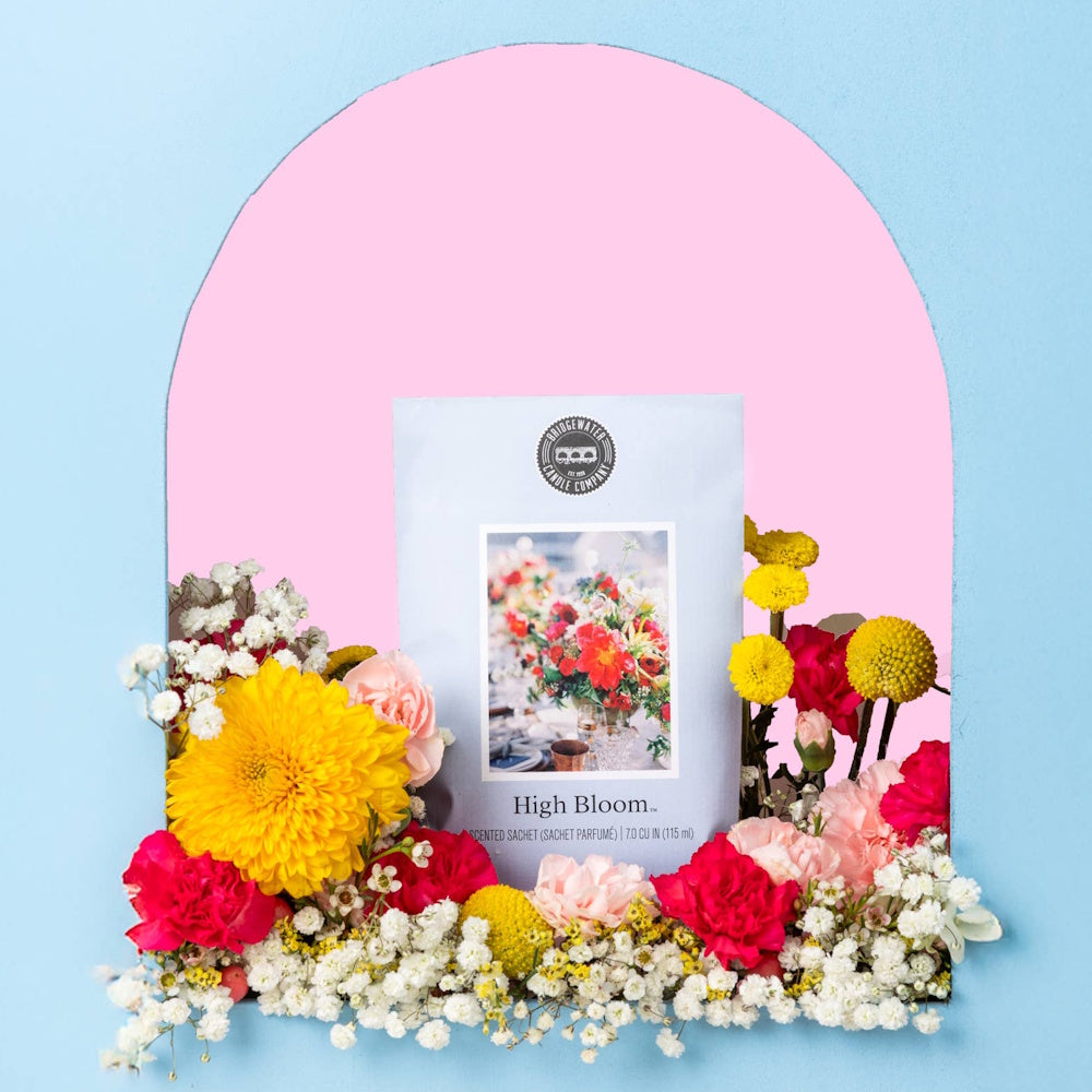Bridgewater Candle Company High Bloom scented sachet surrounded by colorful flowers in a pink and blue arched frame.