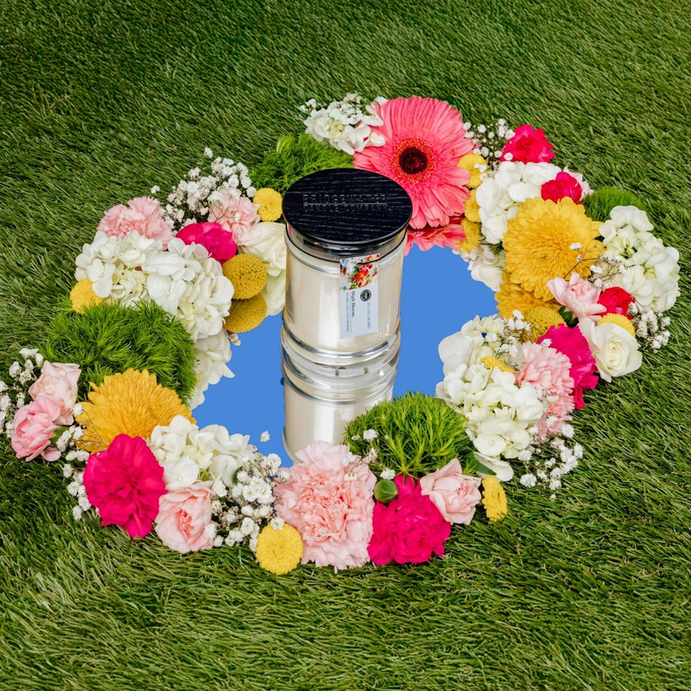 Bridgewater Candle Company High Bloom jar candle on a mirror surrounded by colorful floral wreath on green grass.