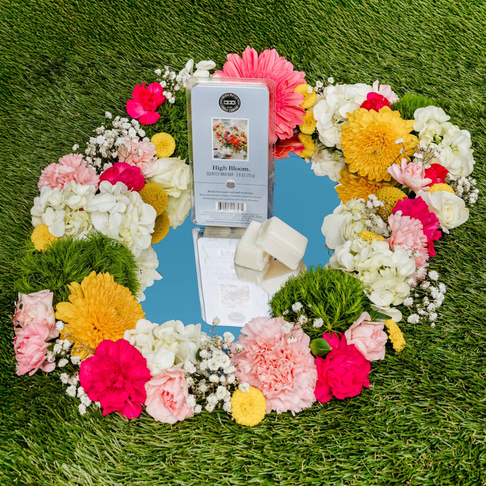 High Bloom scented wax bar by Bridgewater Candle Company on a mirror surrounded by carnations and chrysanthemums.
