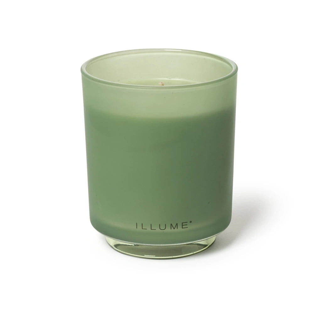 Illume sage green scented candle in a frosted glass jar with a clear glass base, shown against a white backdrop.