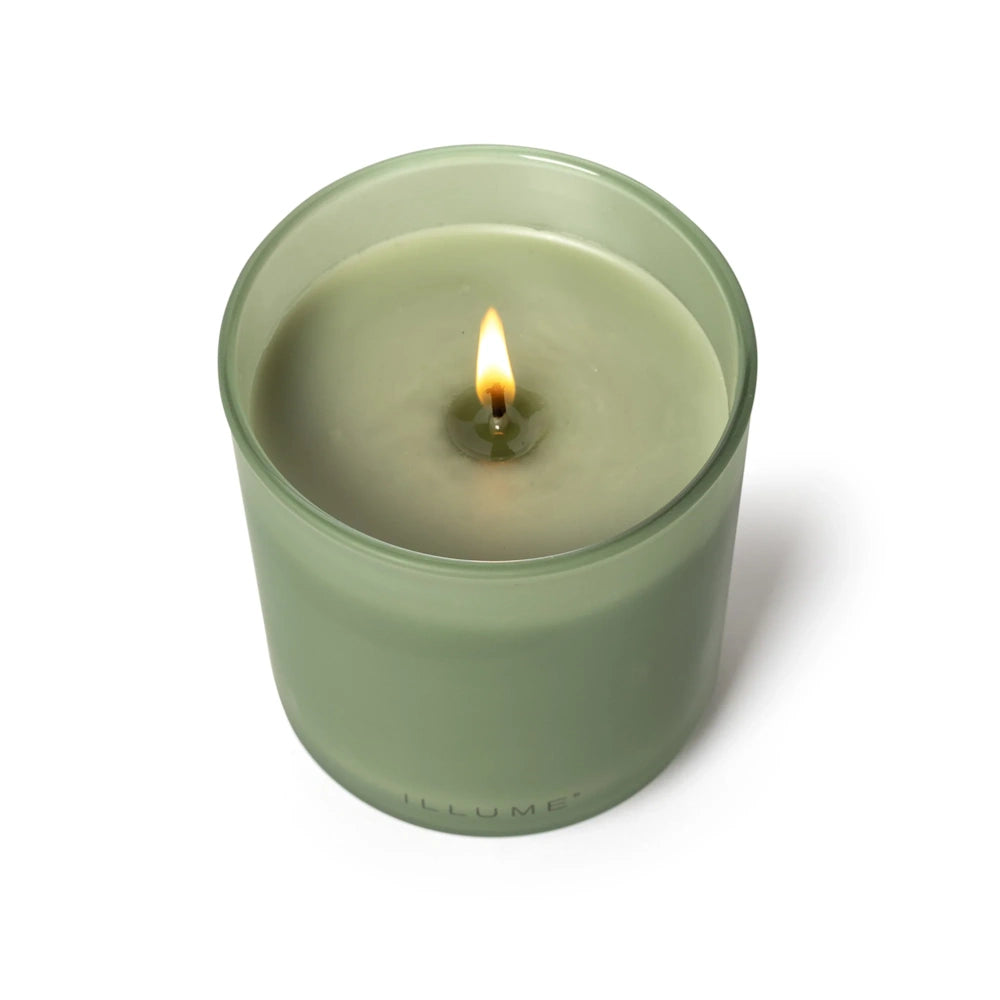 Lit Illume sage green candle in a frosted glass vessel, viewed from above showing the burning wick and melted wax.