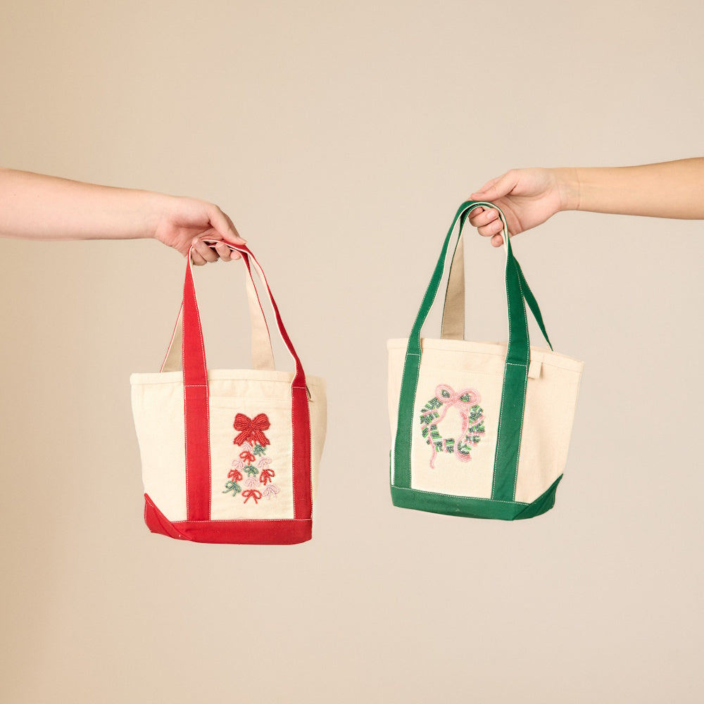 Two people holding holiday beaded mini canvas tote bags with red and green trims.