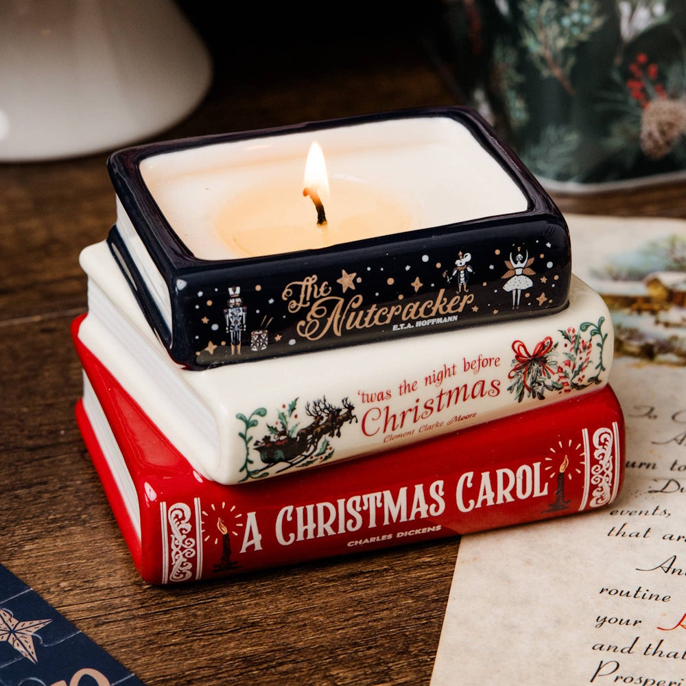 Lit candle set inside a stack of ceramic holiday classic books on a wooden surface.