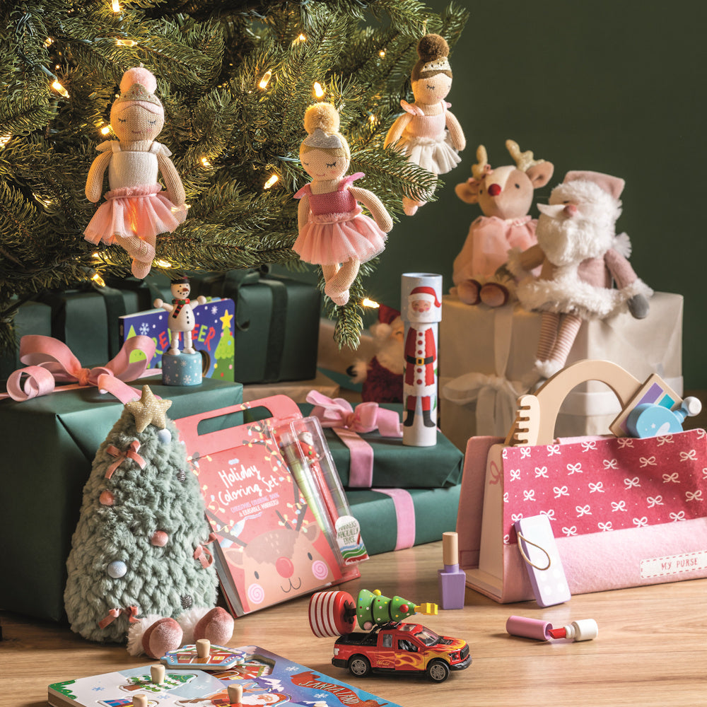 Festive holiday toys and gifts under a lit Christmas tree, featuring ballerina dolls, plush animals, and a coloring set.