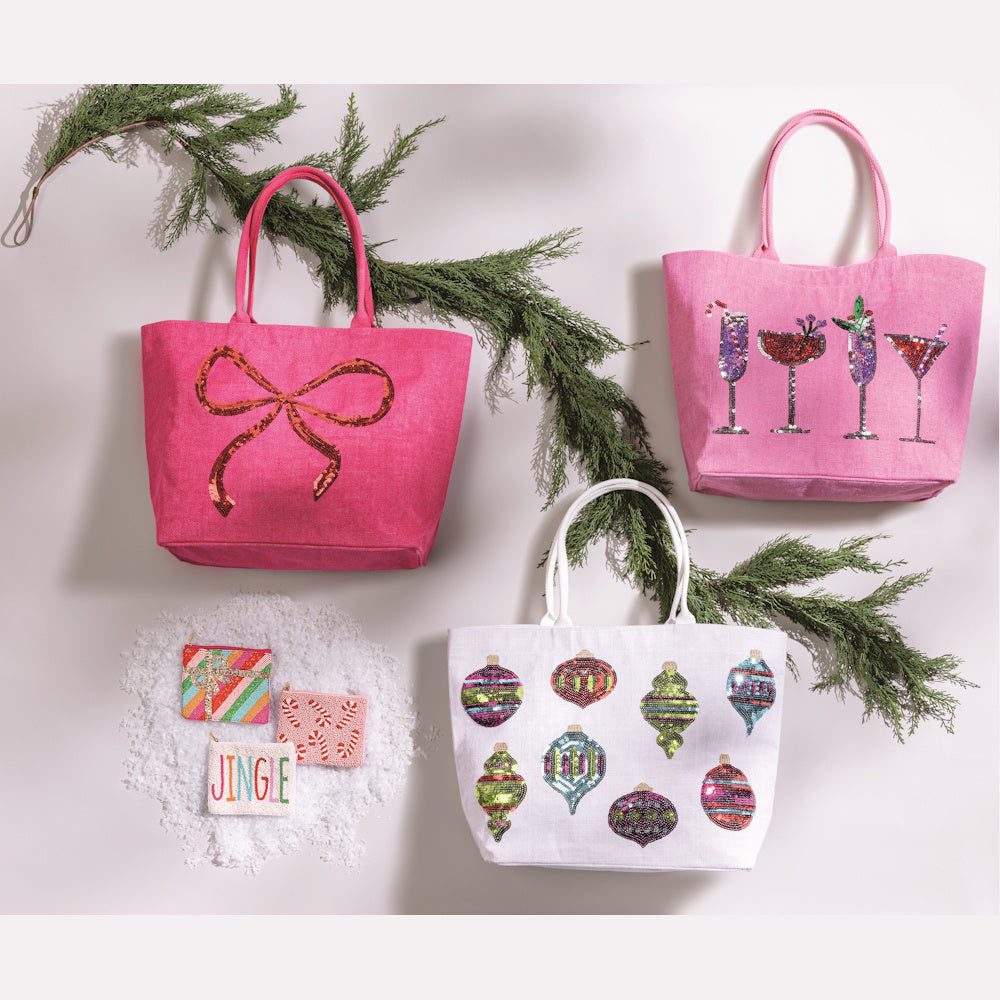 Pink and white holiday tote bags with sequin bows, cocktails, and ornaments alongside beaded festive coin purses.