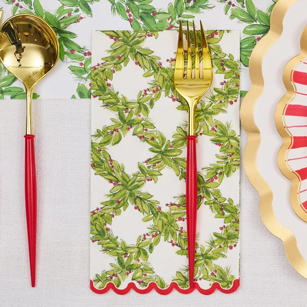 Overhead flat lay of a white paper guest towel with a green holly pattern and red scalloped edge.