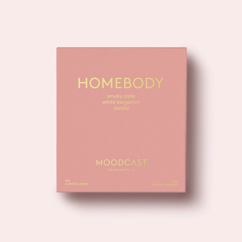 Pink Moodcast Homebody candle packaging box with gold lettering on a light pink background.
