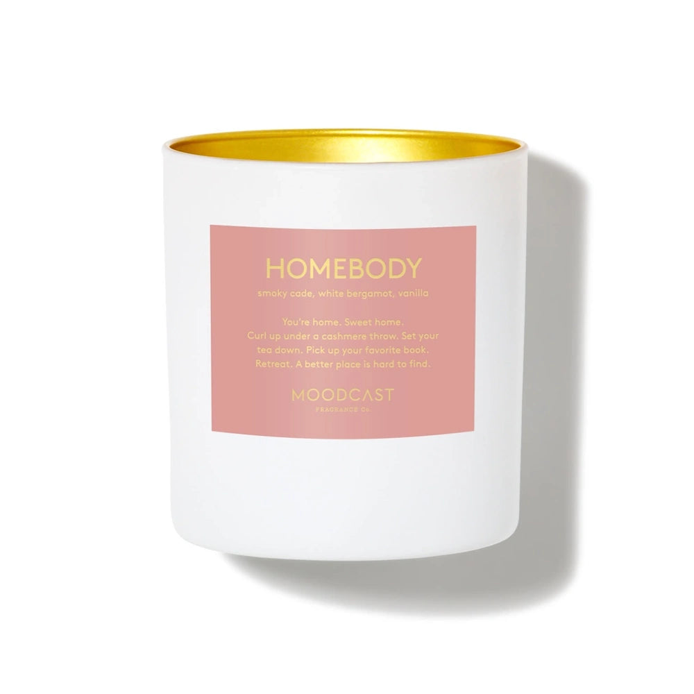 White Moodcast Homebody scented candle in a vessel with a gold rim and a dusty pink label.