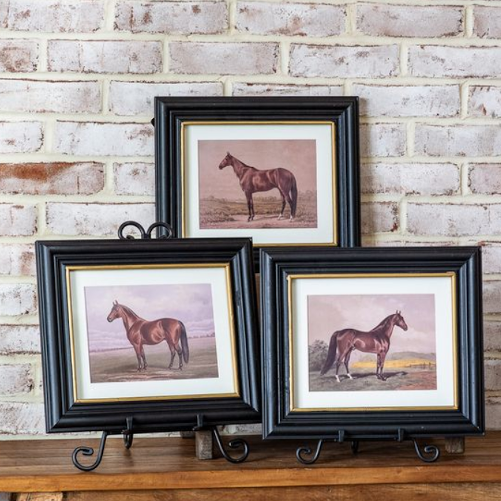 Set of three framed horse art prints in black frames with gold trim displayed against a brick wall.