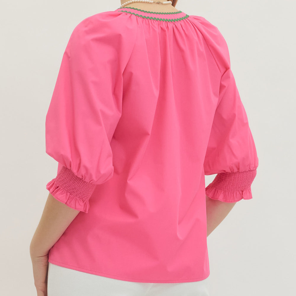 Back view of hot pink blouse with puff sleeves, smocked cuffs and green trim at the neckline.