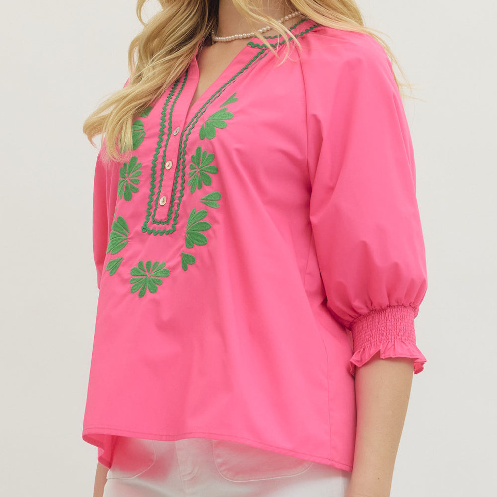Angled view of hot pink blouse with green floral embroidery, split neckline and smocked puff sleeves.