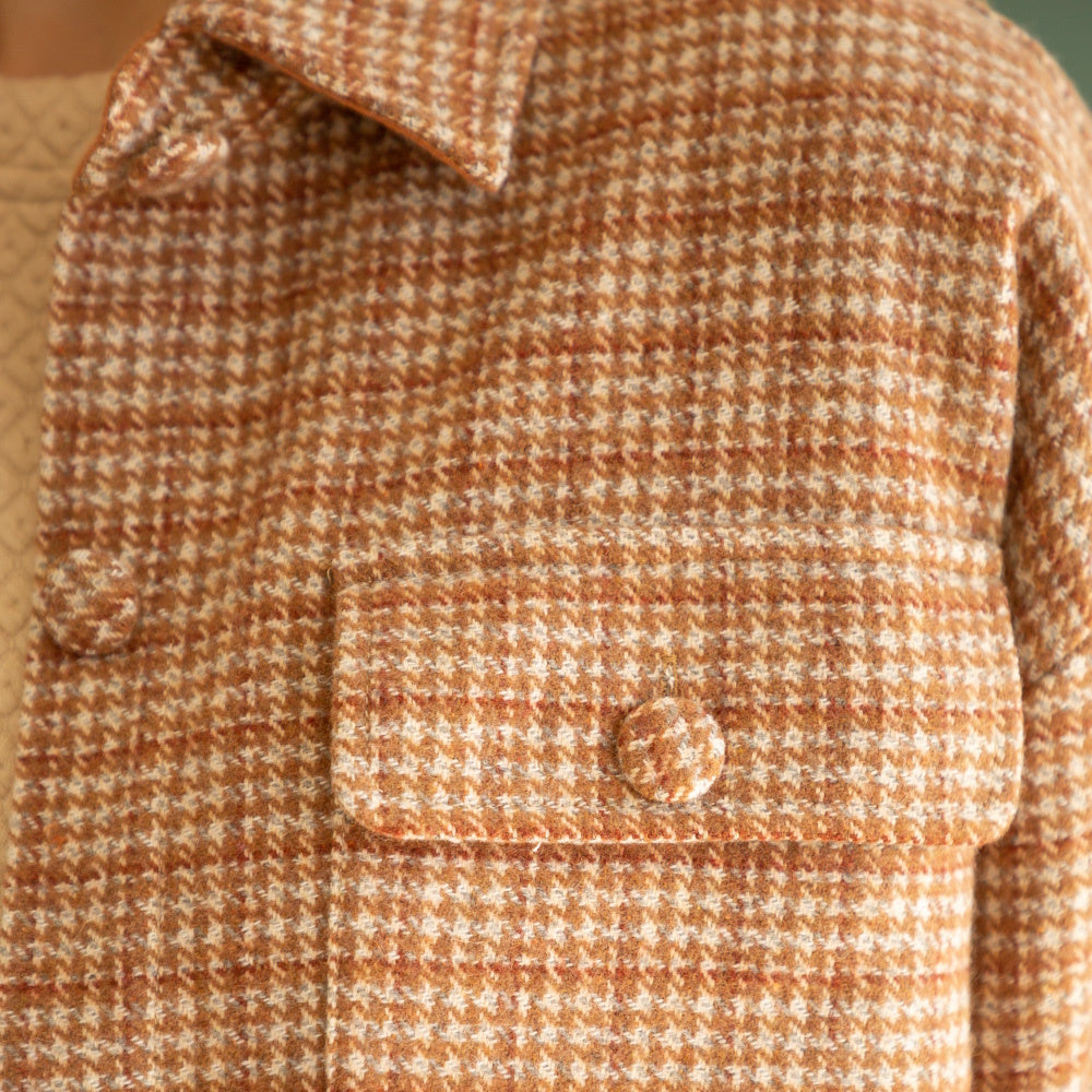 Close-up detail of a brown houndstooth plaid shacket with a buttoned flap pocket and fabric buttons.