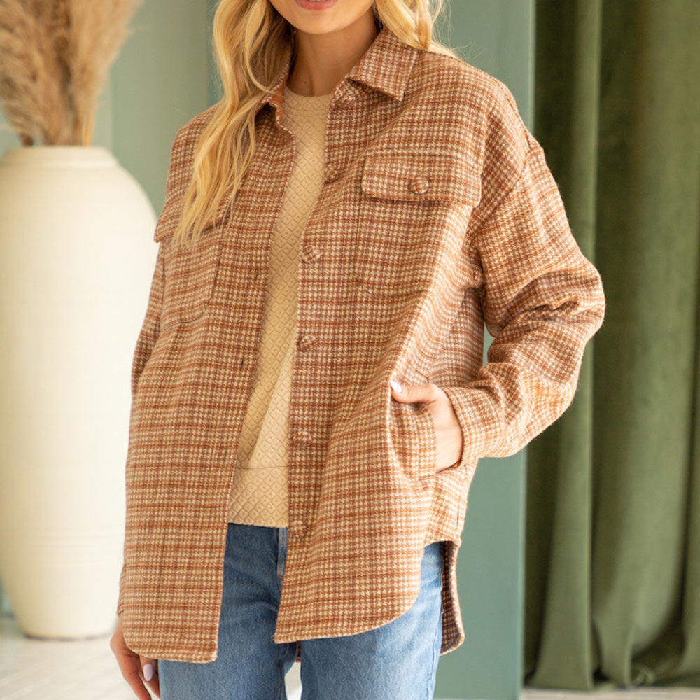 Woman wearing a brown houndstooth plaid shacket with chest pockets over a cream sweater and jeans.