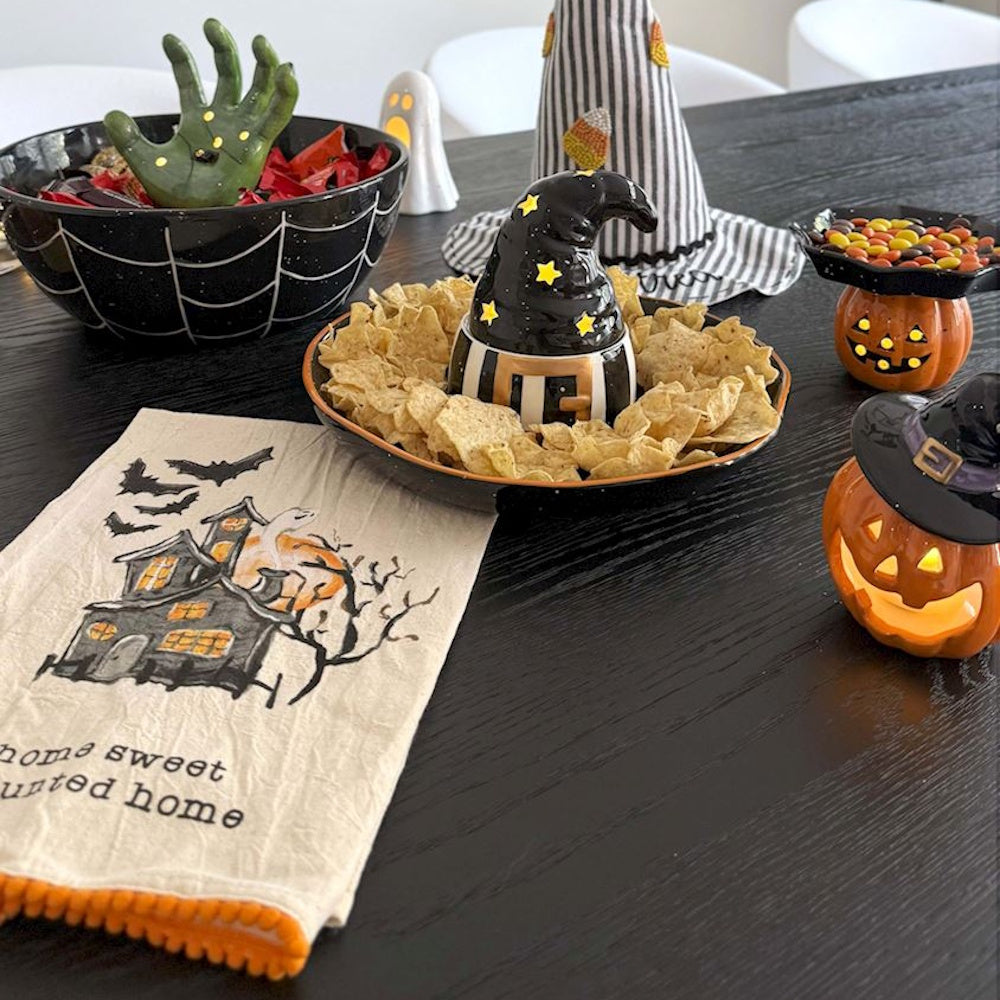 Halloween tea towel with a haunted house graphic on a table with spooky party decorations and snacks.