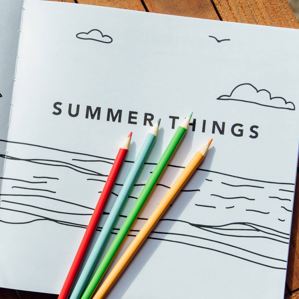 Summer-themed drawing book titled "Summer Things" with colorful pencils on a sketch of ocean waves and clouds.