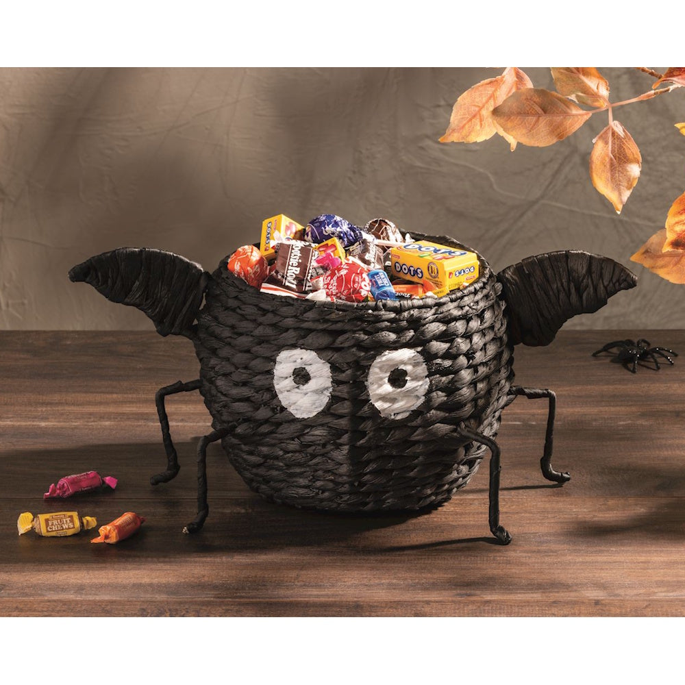 Black woven spider candy bowl filled with Halloween treats on a wooden table.