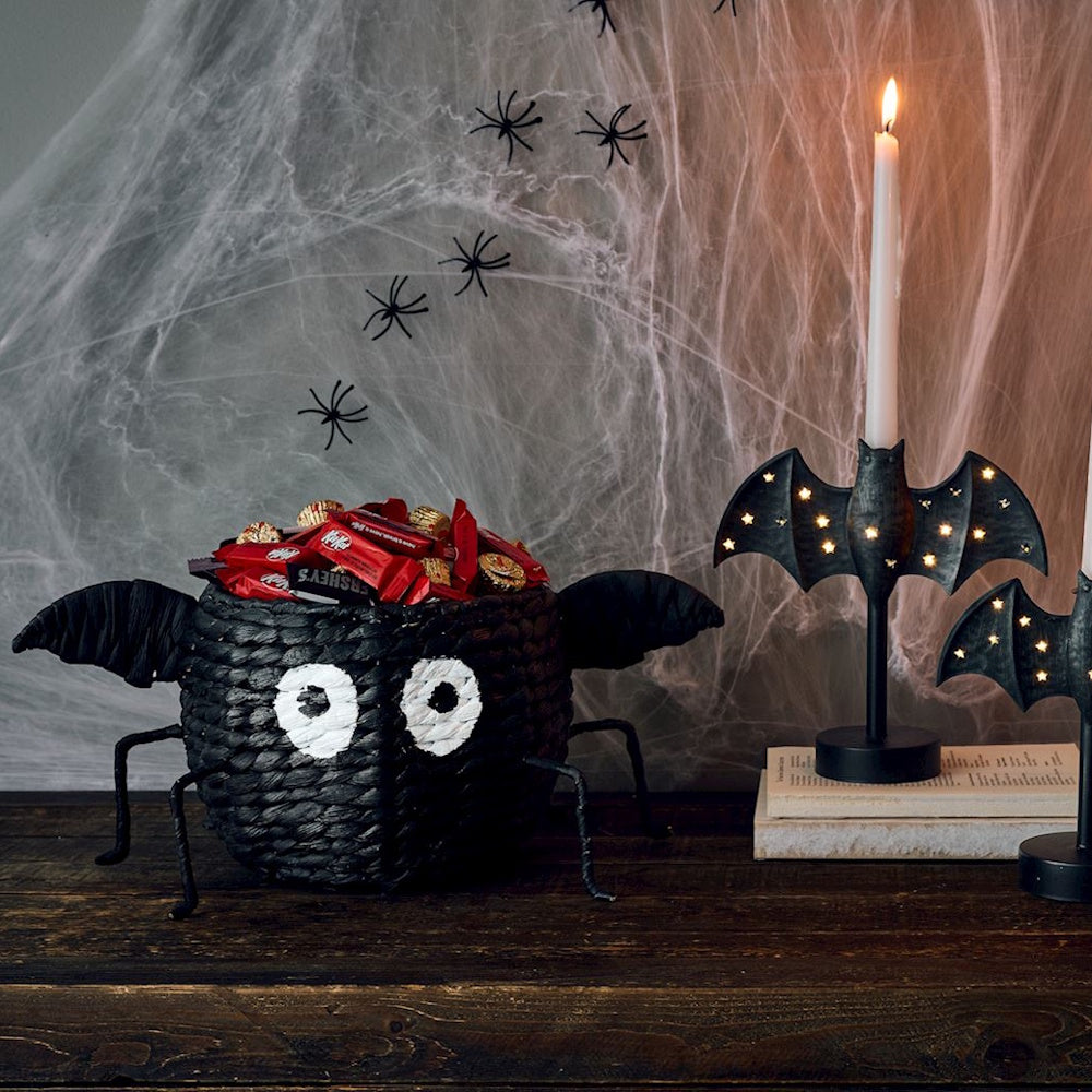 Halloween bat candy bowl on a wooden table next to a bat candle holder.