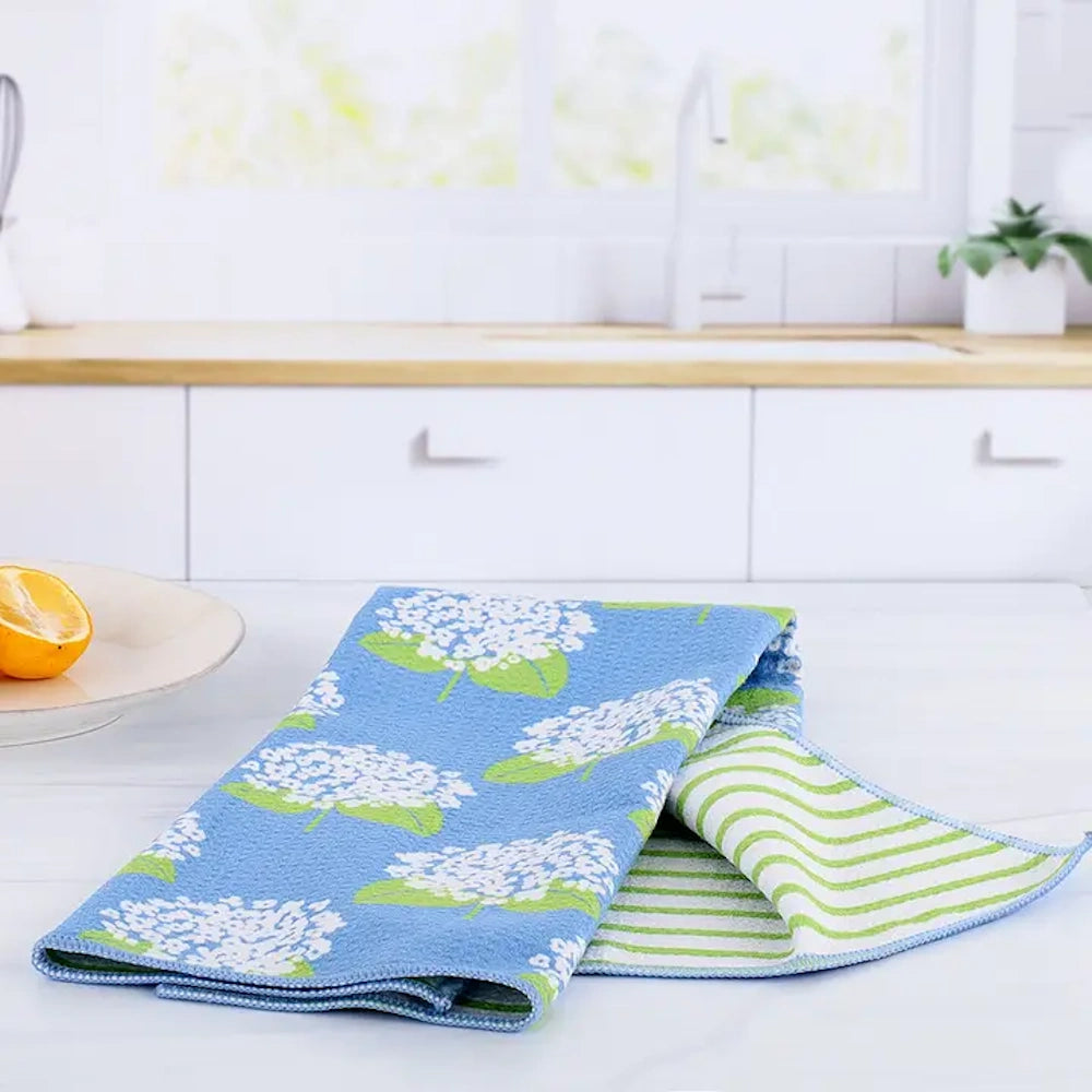Blue hydrangea pattern eco-friendly kitchen tea towel on a white counter with a striped reverse side.