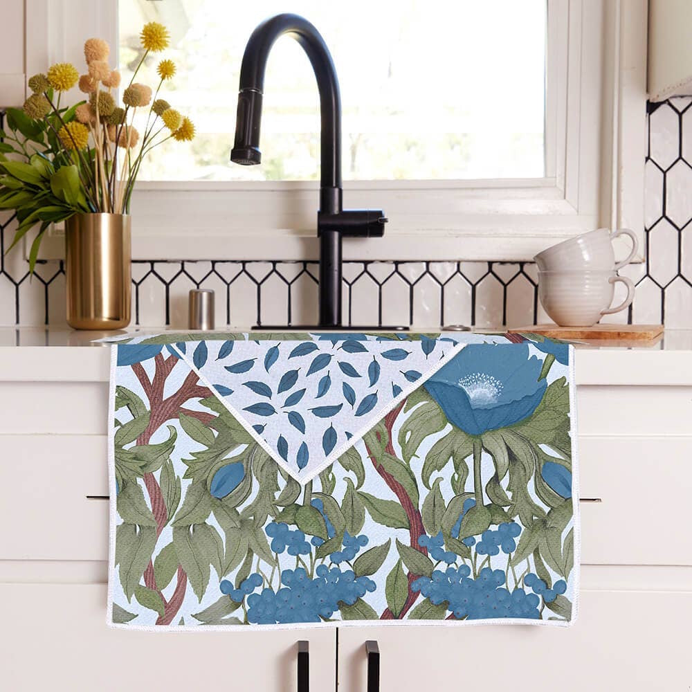 A blue floral kitchen tea towel with a leaf-patterned reverse side hanging over the edge of a kitchen sink.