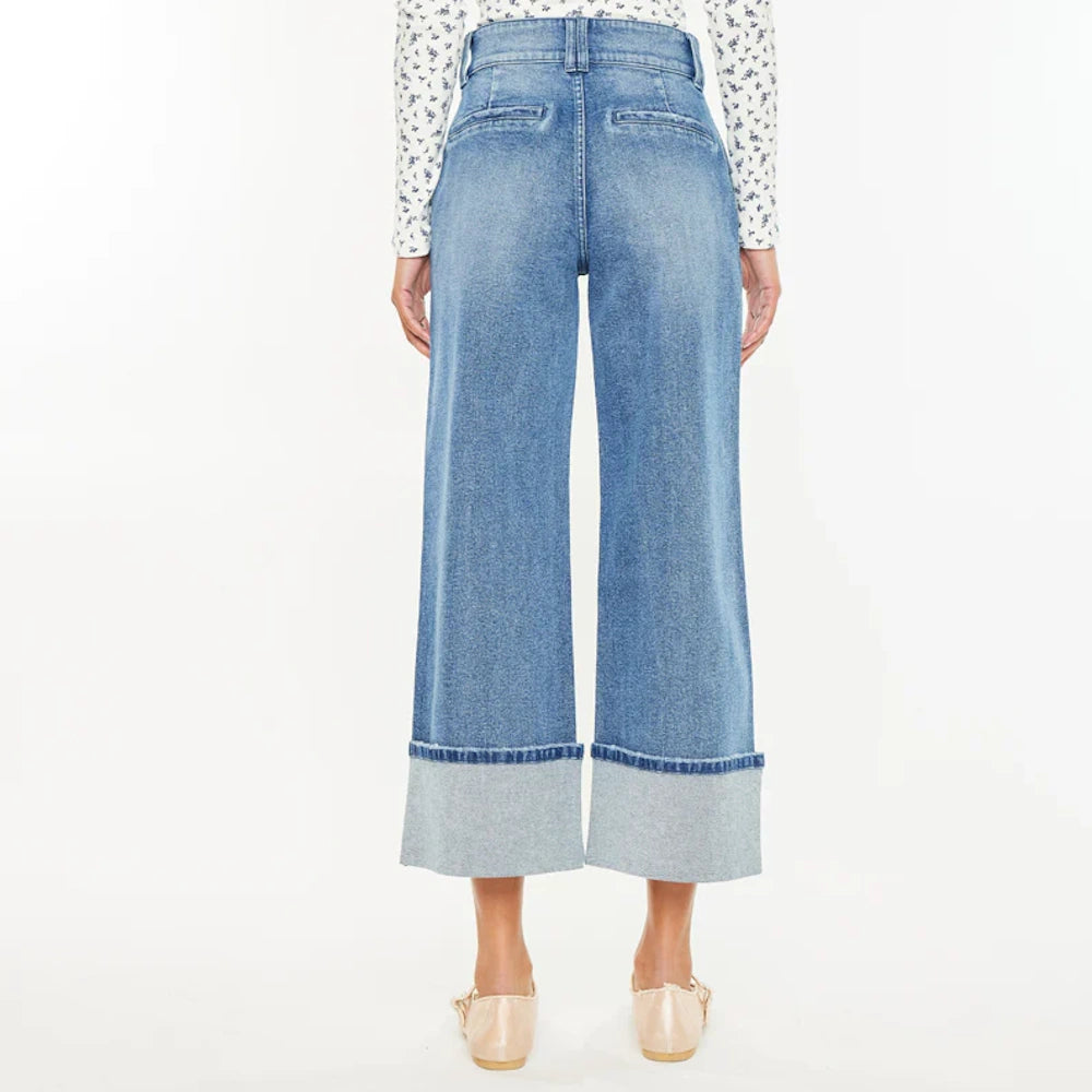 Back view of high-waisted, wide-leg cropped blue jeans with thick cuffed hems and tan ballet flats on a white background.