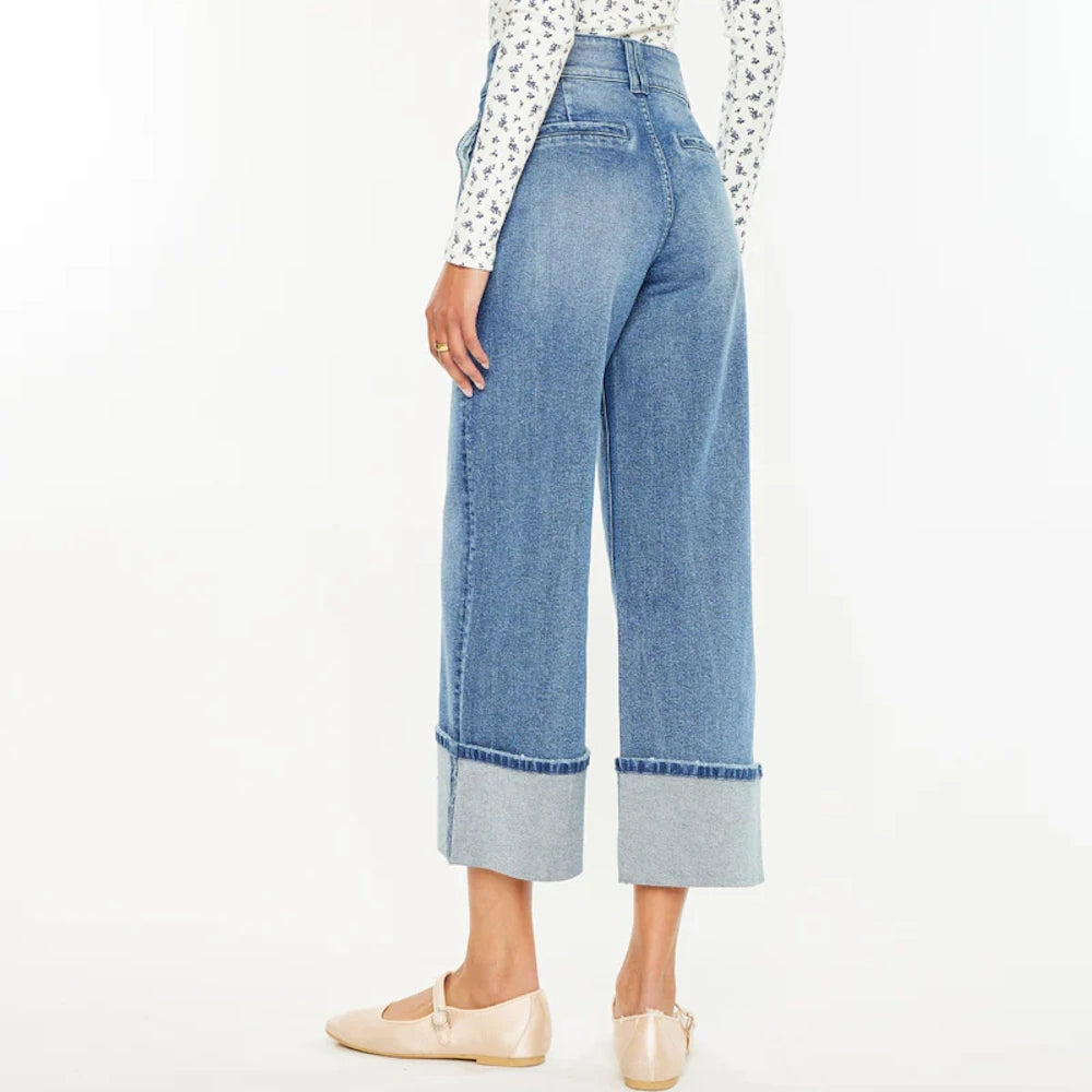 Rear view of a person wearing high-waisted, wide-leg cropped blue jeans with large folded cuffs and tan ballet flats.