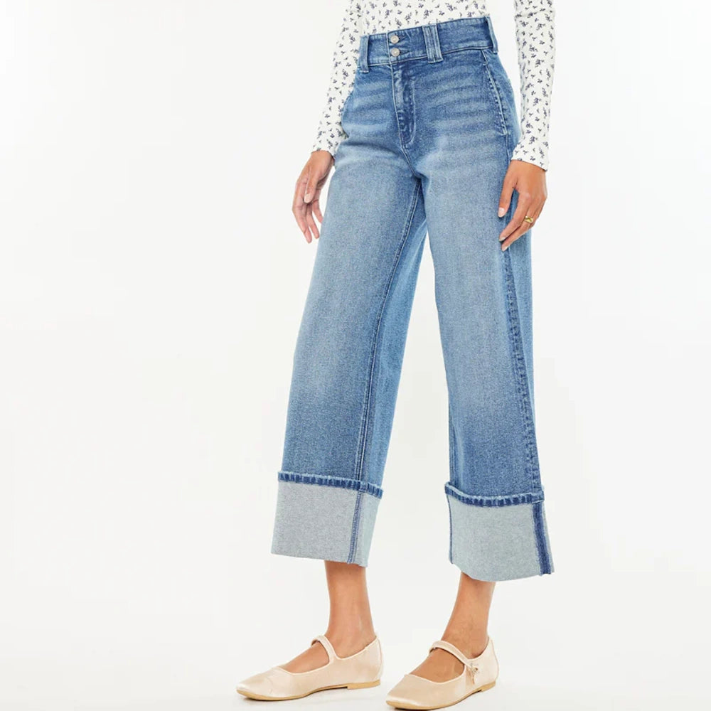Woman wearing high-rise, wide-leg cropped blue jeans with large folded cuffs and tan Mary Jane flats.