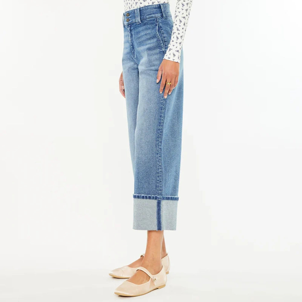 Woman wearing blue high-waisted wide-leg cropped jeans with large folded cuffs and beige Mary Jane flats.